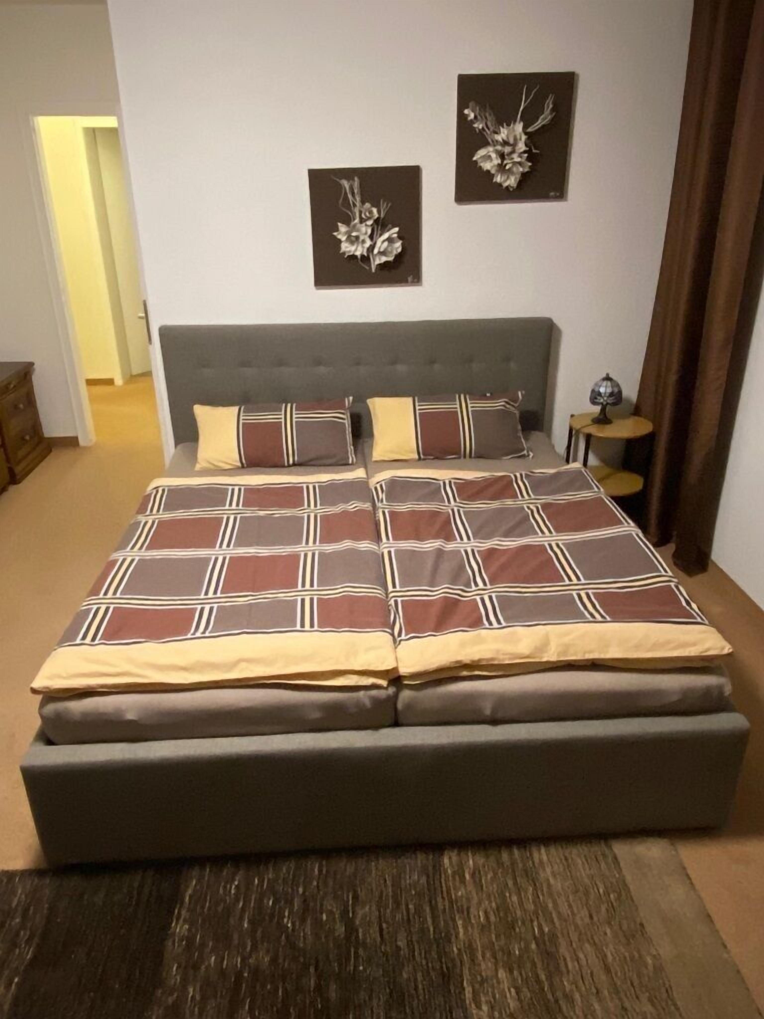 A bedroom with a large bed, two wall-mounted decorative items, a nightstand, and a lamp.