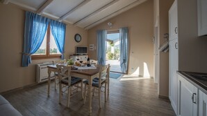 Zona pranzo con tavolo e sedie in legno, televisore e vista sull'esterno attraverso una finestra.