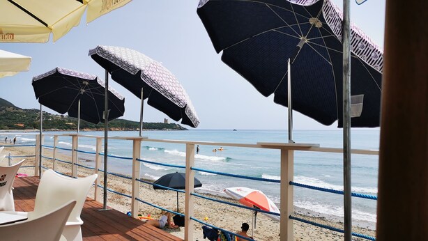 Una terrazza sul mare con diversi ombrelloni, vista sul mare e persone sulla spiaggia sullo sfondo.