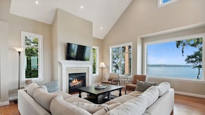 A living room with a fireplace, a television, and a large window overlooking a body of water.