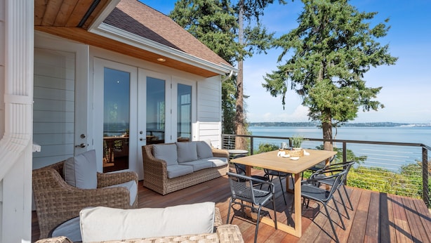 A deck with wicker furniture, a wooden table, and a view of the water.