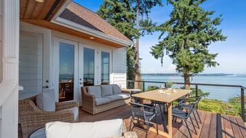 Une terrasse dotée de meubles en osier, d’une table en bois et offrant une vue sur l’eau.