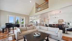 A spacious living room with a sectional sofa, a piano, and a dining area with a chandelier.
