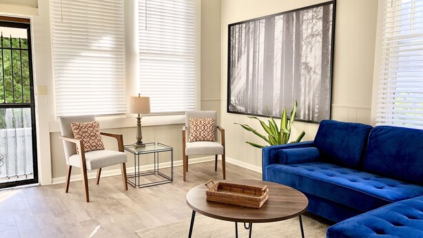 Ein Wohnzimmer mit einem blauen Sofa, zwei Sesseln, einem Couchtisch und einem großen Gemälde an der Wand.