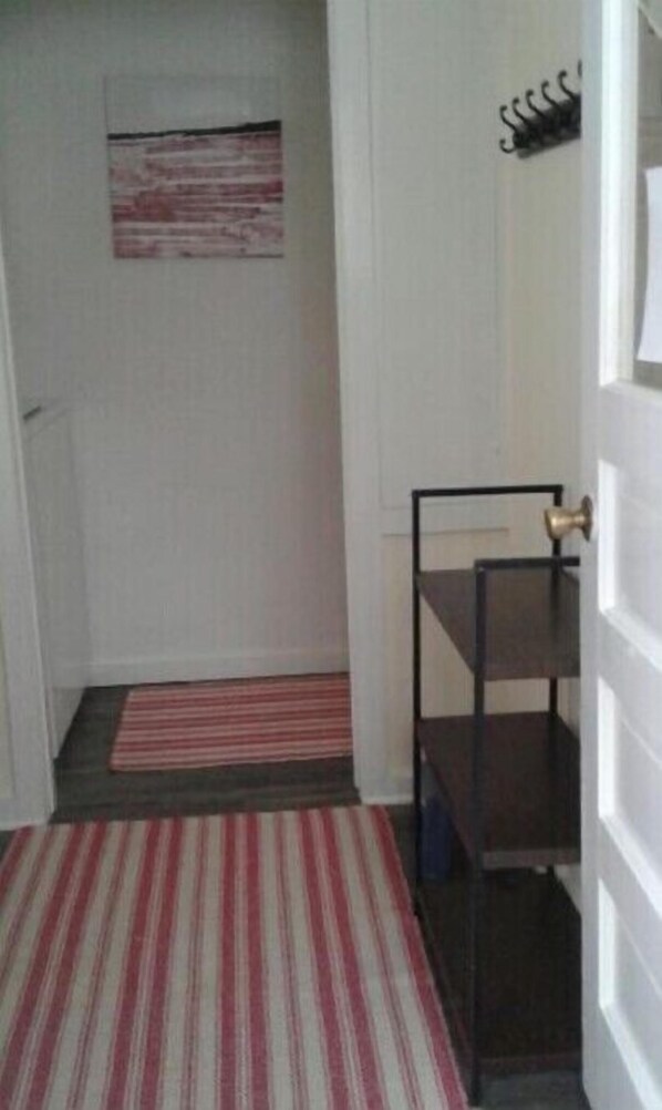 A narrow hallway with a striped rug leading to a door. A small shelf unit is visible to the right. - The Penny House: CLEAN with garage, one block from trails & stores
(Bruce Crossing)