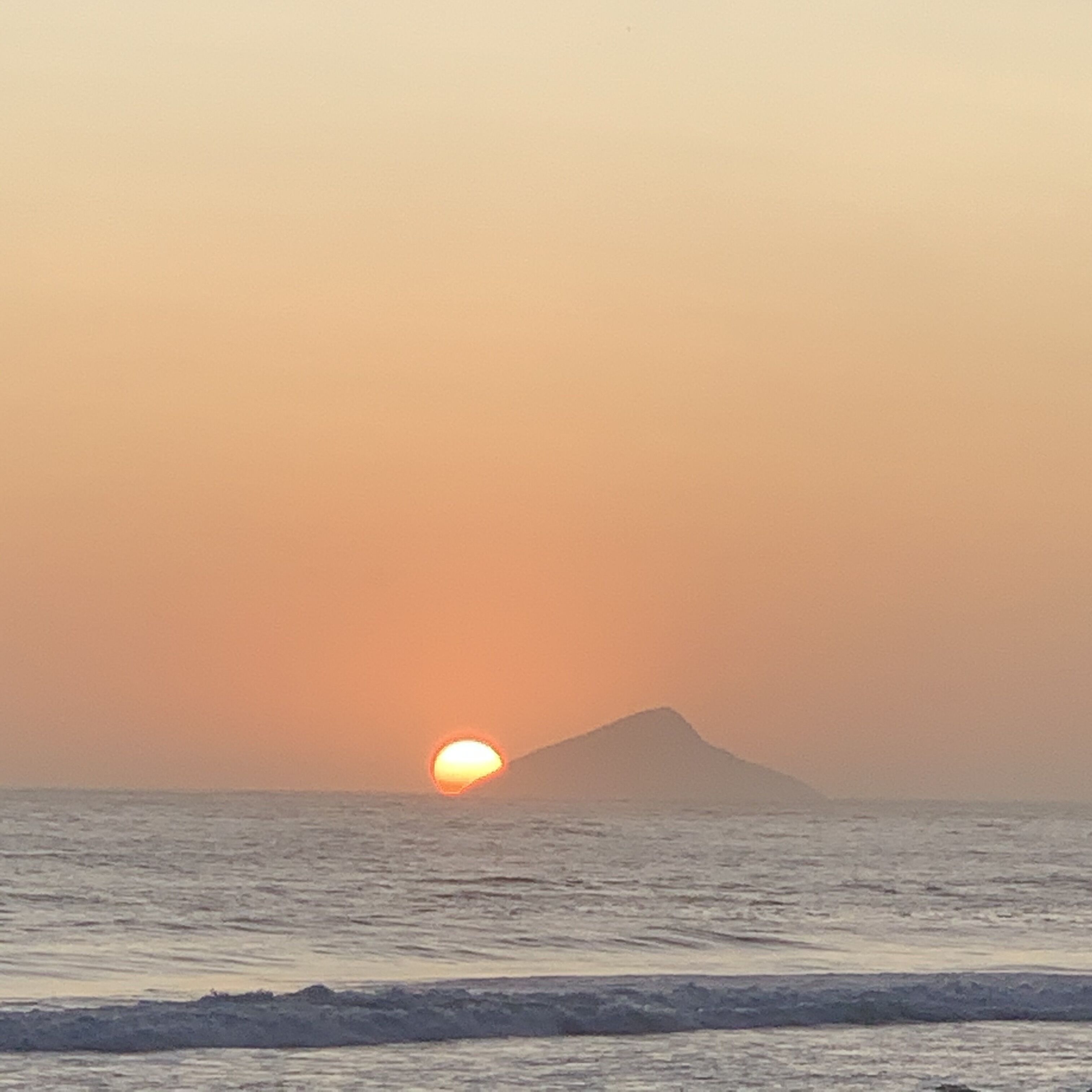 Um pôr do sol sobre o oceano, com uma montanha ao longe.