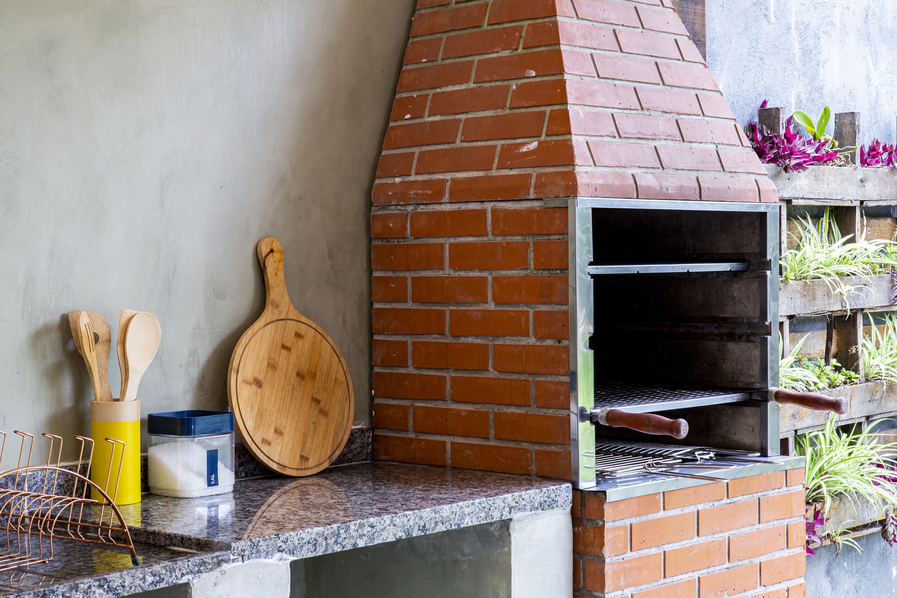 A brick oven with a metal rack, wooden utensils, and a cutting board on a countertop.