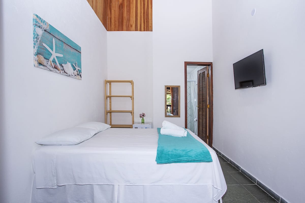A bedroom with a bed, a wooden ladder, a TV, and a painting on the wall.