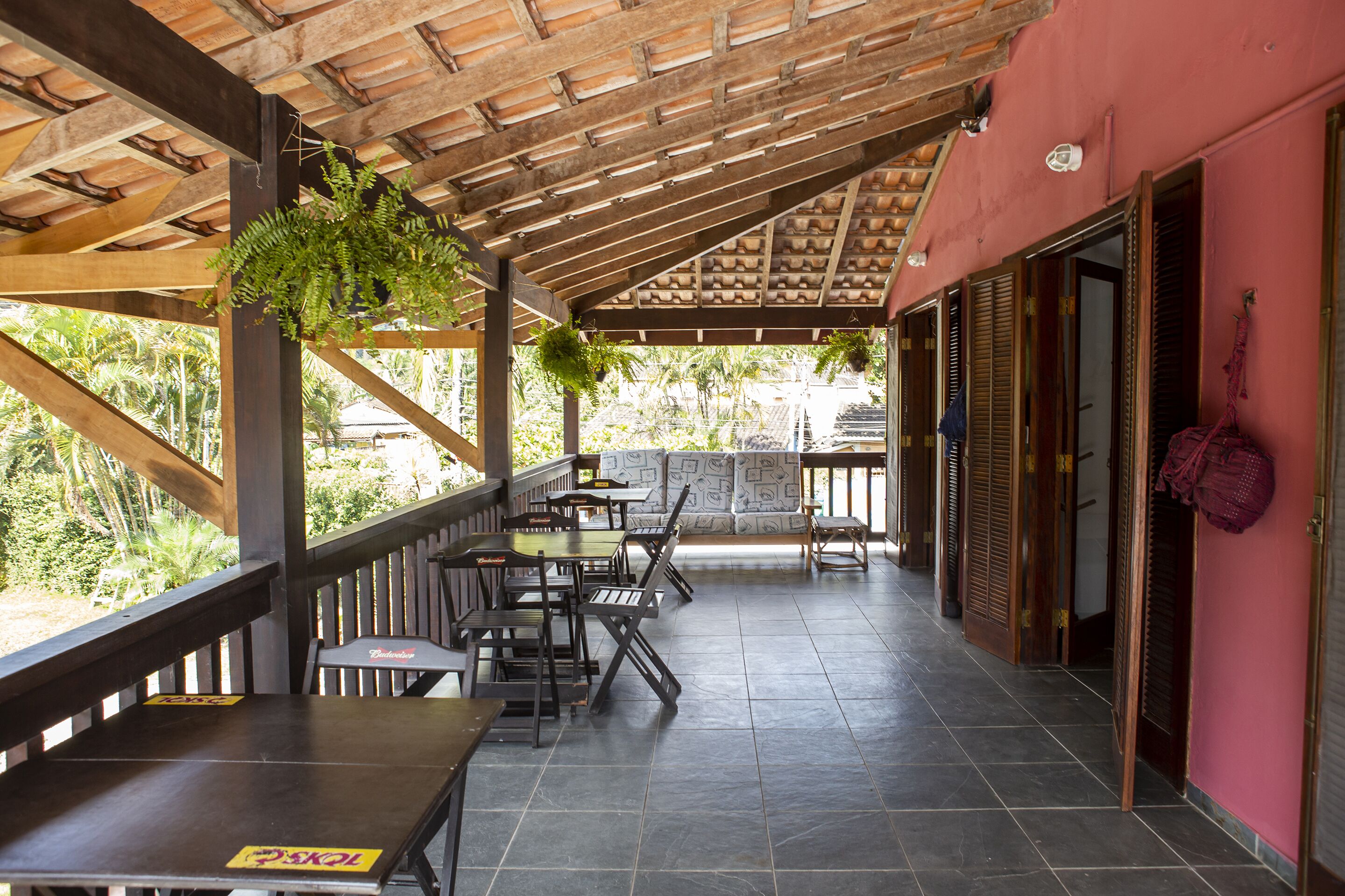 Un espace extérieur aménagé en terrasse, avec des tables et des chaises en bois, une fougère suspendue et une vue sur la verdure environnante.