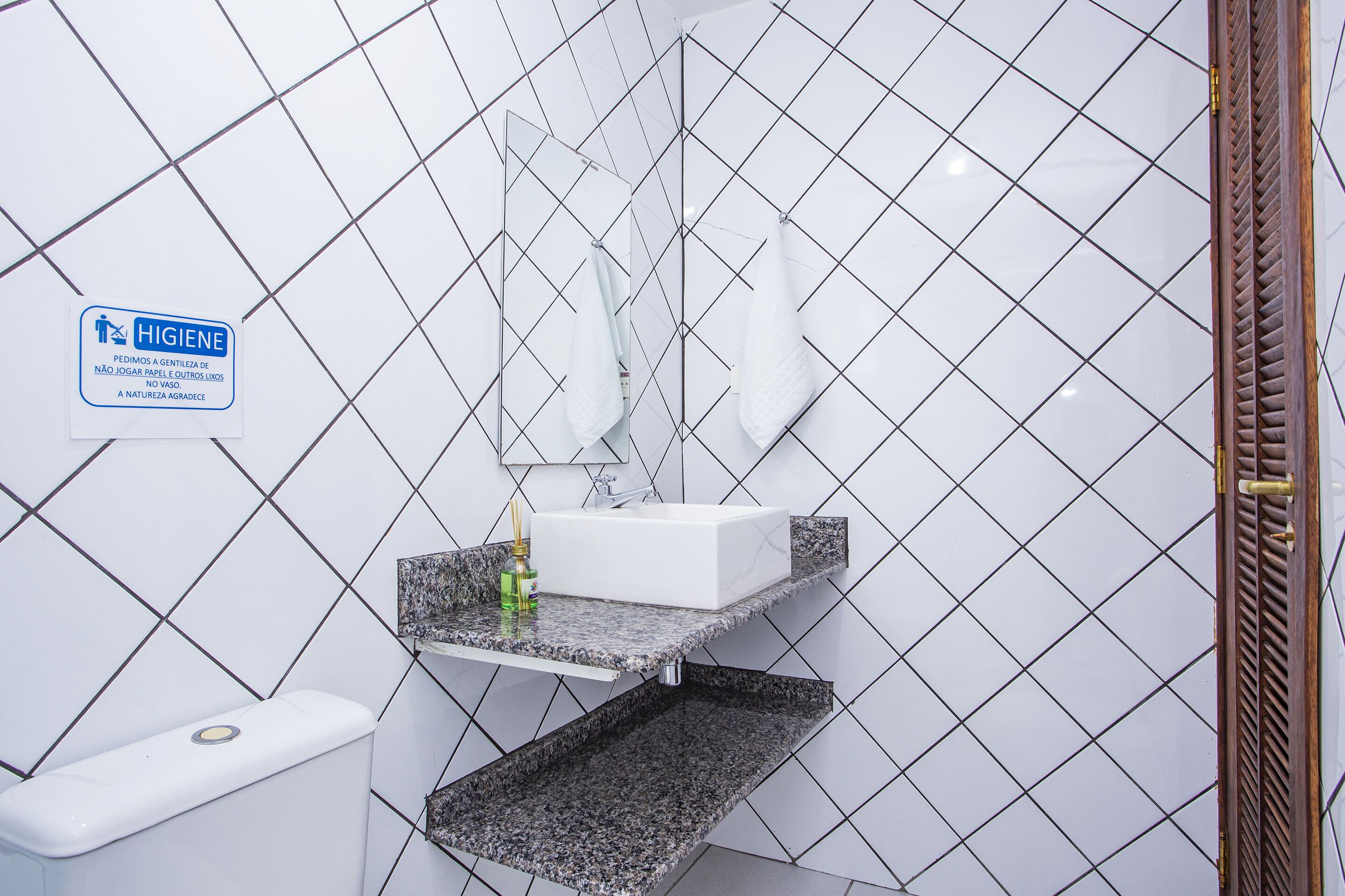 Een badkamer met een witte betegelde muur, een wastafel met spiegel en een handdoekhouder.