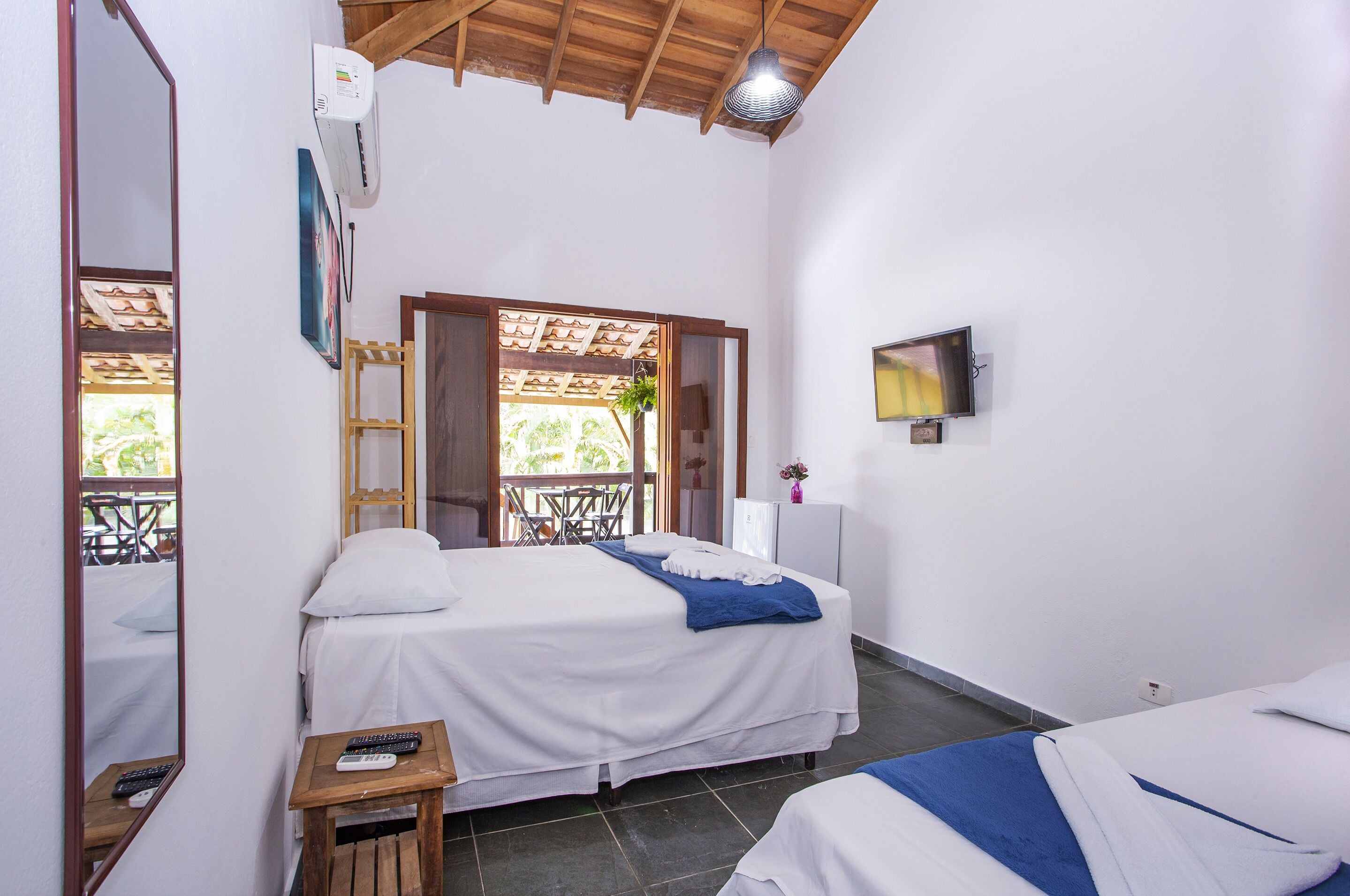 A bedroom with two beds, a TV, a mirror, and a small table with a remote control.