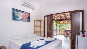 A hotel room with a bed, a blue towel, a wooden shelf, an air conditioner, and a balcony with a table and chairs.