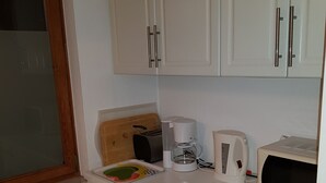 A small kitchen with white cabinets, a wooden countertop, a toaster, a kettle, and a microwave. - Hansa Apartments Hamburg - Apartment 1B (Wandsbek)