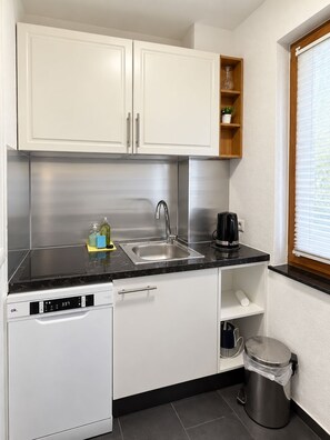 Een praktische keuken met witte kastjes, een RVS spoelbak, een koffiezetapparaat en een vaatwasser.
