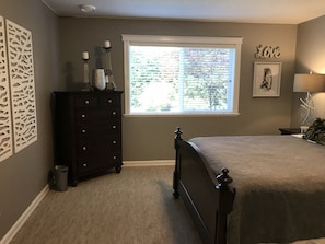 A bedroom with a bed, dresser, window, and decorative wall pieces.