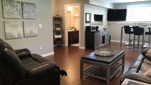 A living room with a leather sofa, a coffee table, and a dining area with a TV and chairs. - Lower Level Entry Home with private Patio & back yard. (Nanaimo)