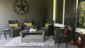 A covered patio area with a seating arrangement including a sofa and chairs, a coffee table, and decorative plants. - Lower Level Entry Home with private Patio & back yard. (Nanaimo)