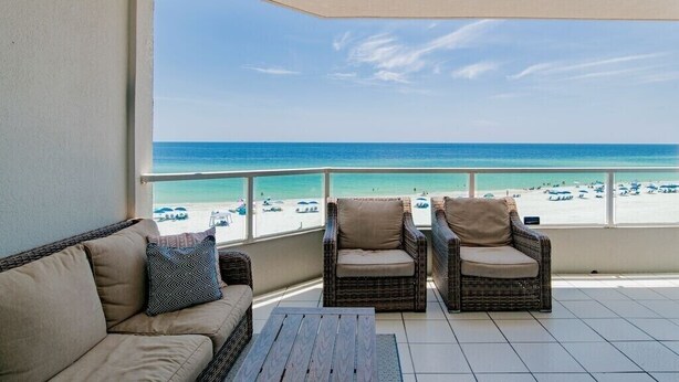 A balcony with wicker furniture, a view of the beach, and a clear sky. - Silver Beach 402 | Updated, Direct Beach Front, Pet Friendly! (Orange Beach)