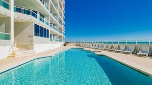 A pool area with a clear blue pool, white lounge chairs, and a building with balconies. - Silver Beach 402 | Updated, Direct Beach Front, Pet Friendly! (Orange Beach)
