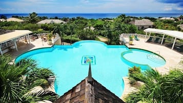 Ein großer, klarer Swimmingpool mit Blick auf den Ozean, umgeben von üppiger Vegetation und einer überdachten Sitzgelegenheit.