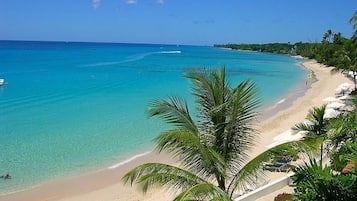 Ein Strand mit klarem türkisblauem Wasser, einem sandigen Ufer und Palmen.