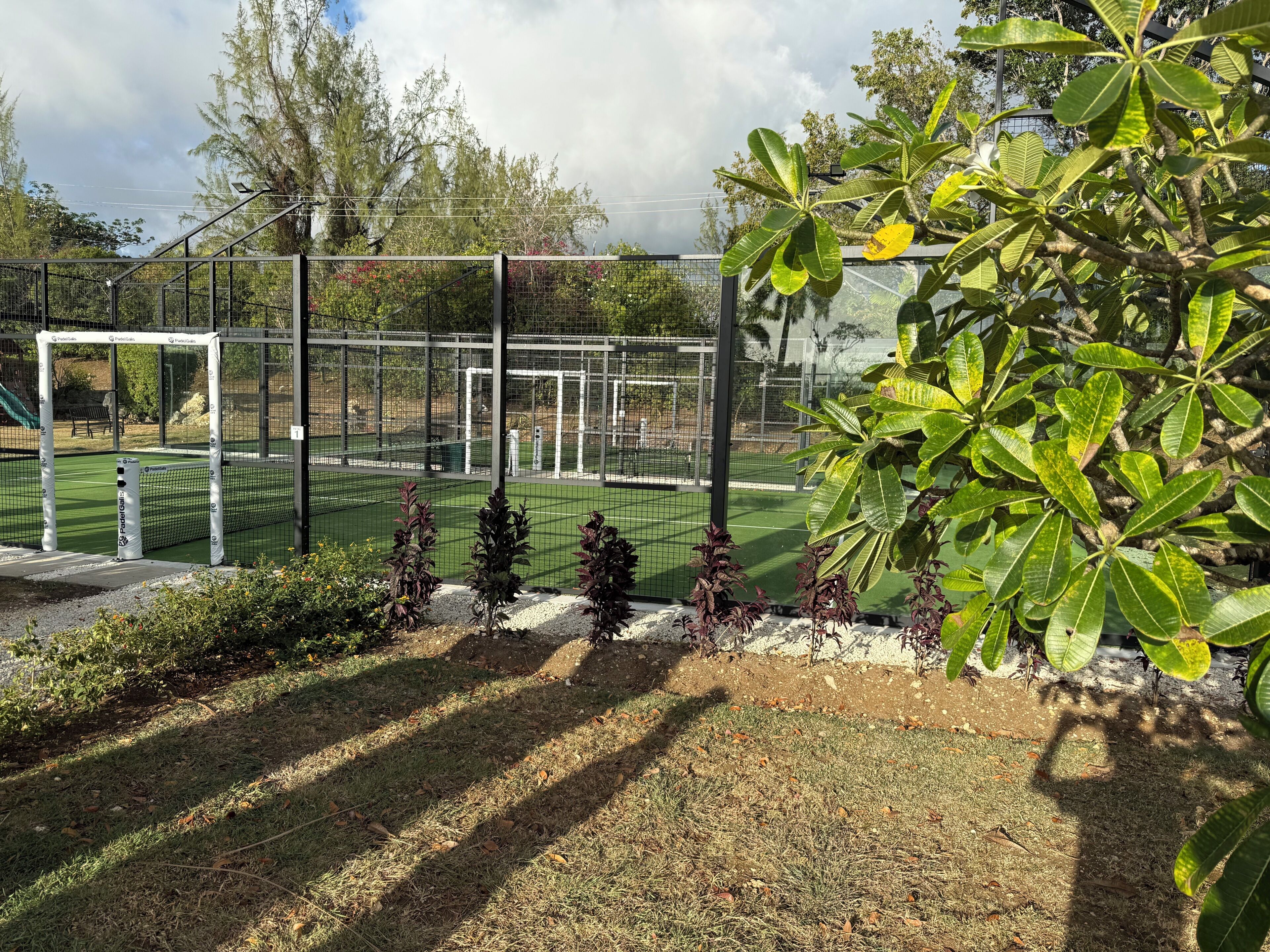 Un espace sportif clôturé, doté d’une pelouse artificielle, de poteaux de but et entouré de verdure.