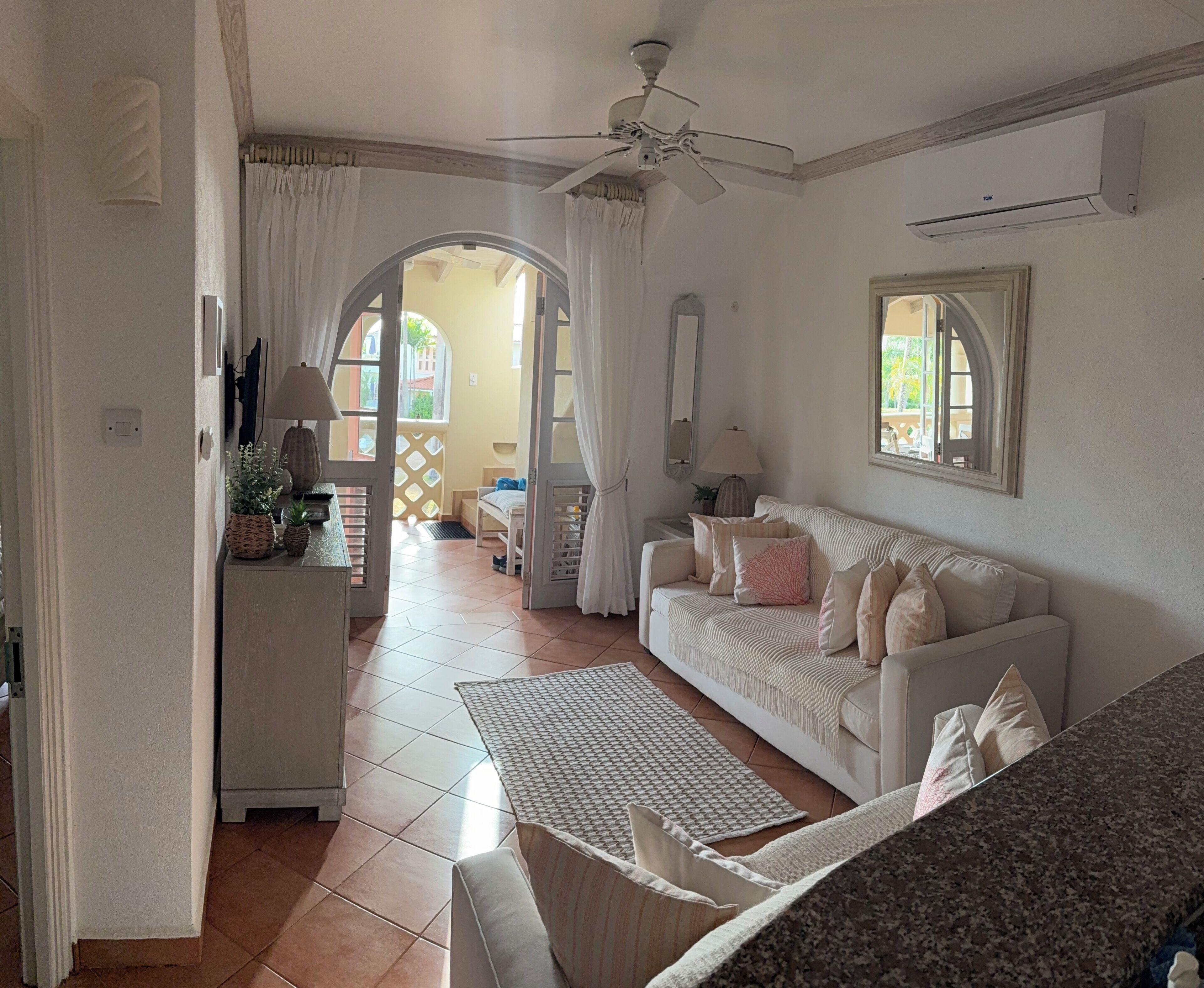 Ein Wohnzimmer mit einem weißen Sofa, einem Couchtisch, einem Deckenventilator und einem Fenster mit Vorhängen.