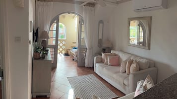 Ein Wohnzimmer mit einem weißen Sofa, einem Couchtisch, einem Deckenventilator und einem Fenster mit Vorhängen.