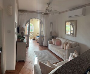 Sala de estar com sofá branco, mesa de centro, ventilador de teto e janela com cortinas.