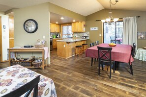 A spacious kitchen with wooden cabinets, a central island, and a dining area with a red tablecloth. - Modern Home Near Fort Rock. SHARC Passes included. Dog Friendly With Pet Fee (Sunriver)