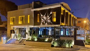 Un hotel moderno con una entrada destacada, zona de estar al aire libre y un letrero que indica el nombre "Hotel Rudis".