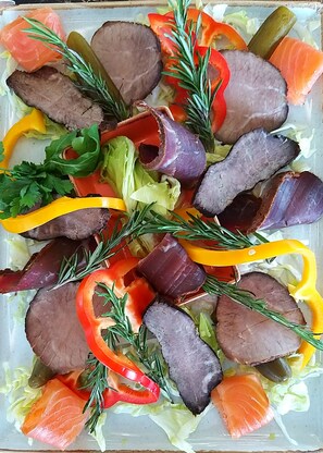 A platter of sliced meat, vegetables, and herbs.