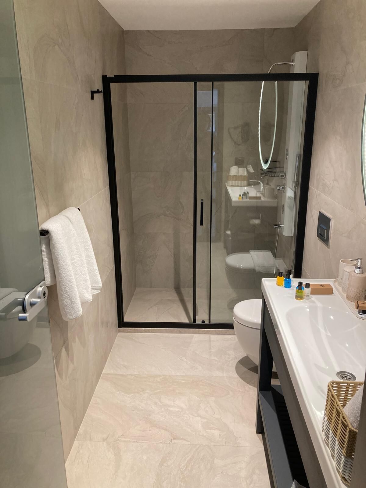 A modern bathroom with a glass-enclosed shower, a white sink with toiletries, and a towel rack.