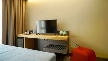 A hotel room with a bed, a desk with a television, a coffee maker, and two water bottles.