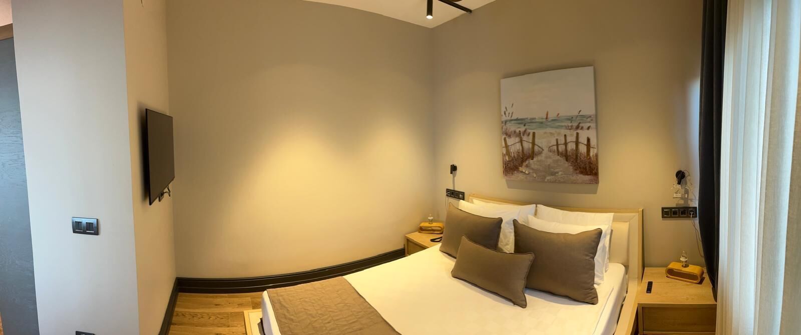 A bedroom with a bed, bedside tables, a flat-screen TV, a painting on the wall, and a power outlet.