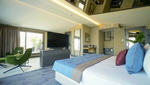 Habitación de hotel moderna con una cama grande, un televisor de pantalla plana, un escritorio y una zona de estar con sillas verdes.