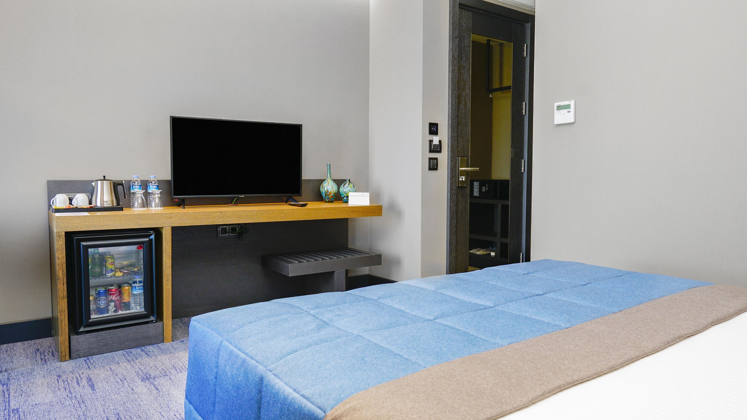 A hotel room with a bed, a small fridge, a television, a coffee maker, and a minibar.