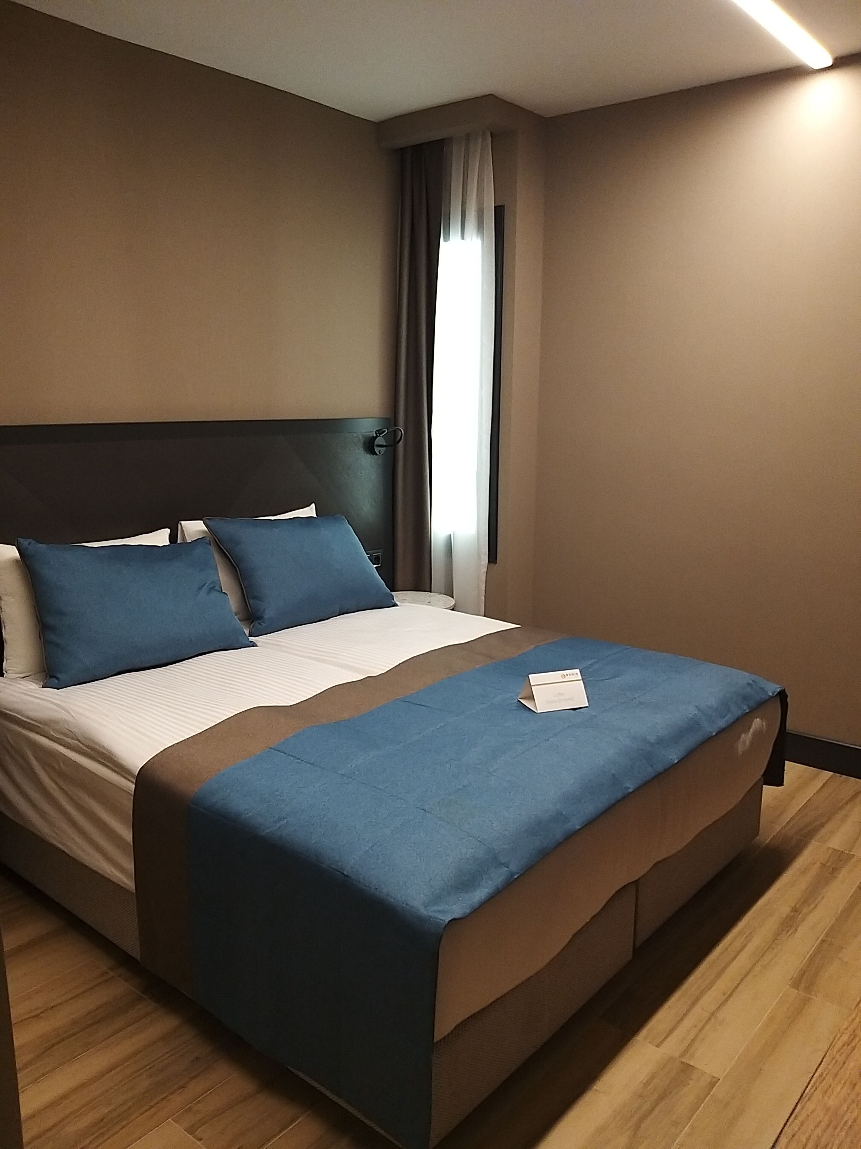 A neatly made bed with blue and white bedding, a dark headboard, and a wooden floor.