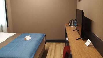 A hotel room with a bed, a desk with a computer, a chair, and a TV.