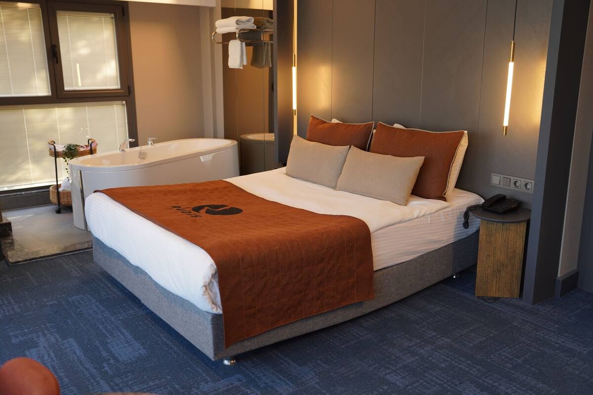 A modern hotel room with a large bed, a built-in bathtub, and a small bedside table with a phone.