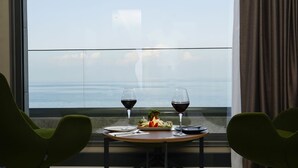 Una mesa con dos copas de vino y un plato de comida junto a una ventana con vista al mar.