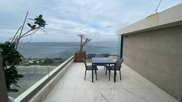 A balcony with a table and chairs, overlooking a body of water and distant land.