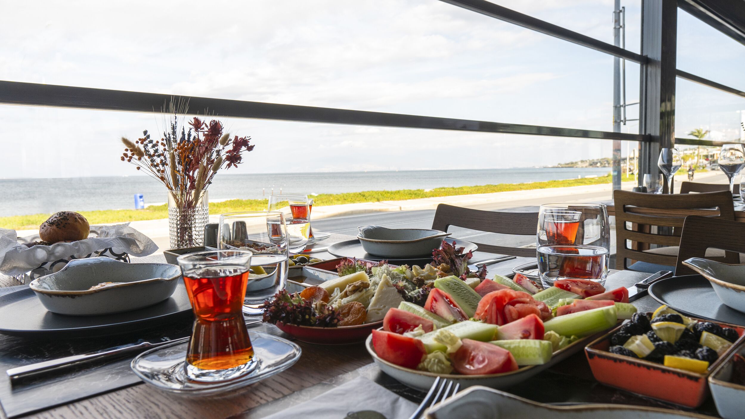Mesa servida con diversos platos y bebidas, con vista al mar.