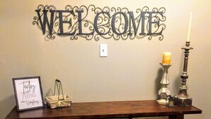 A wooden console table with a 'WELCOME' sign above it, a framed sign saying "Today I'm excited about everything", and a candle holder with a candle. - Loft Apartment - Manitou (Manitou Springs)