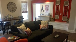A living room with a sofa, coffee table, and red armchair. There is a dining table with chairs in the background. - Loft Apartment - Manitou (Manitou Springs)