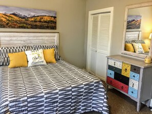 Een slaapkamer met een bed met een geborduurde spreideken, hoofdeinde en een dressoir met meerdere lades.