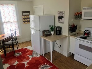 Een compacte keuken met een koelkast, fornuis, magnetron en een klein eethoekje met een tafel en stoelen.
