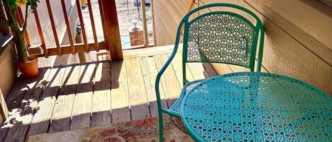 A wooden deck with a turquoise metal table and chairs, a potted plant, and a patterned rug.