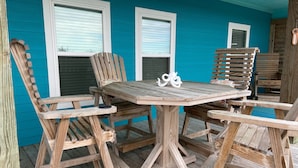 Una terraza de madera con una mesa y sillas, rodeada de paredes azules y ventanas.