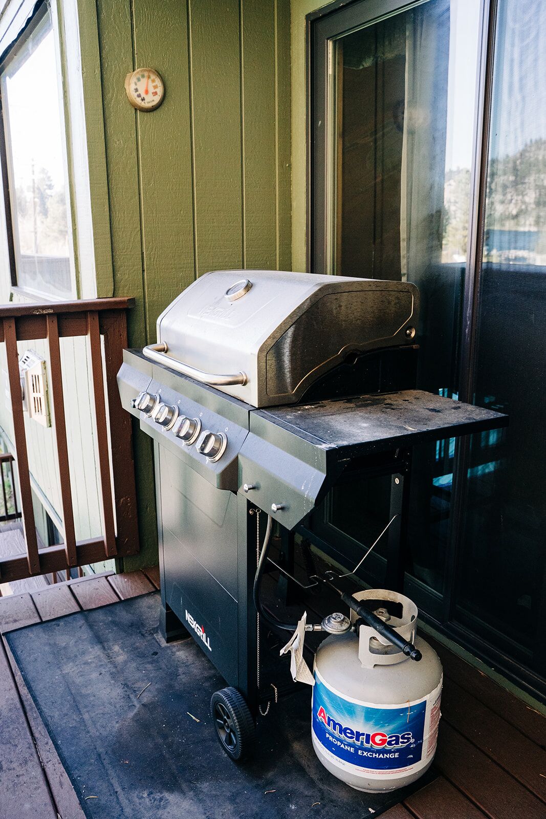 A portable grill with a propane tank on a porch.